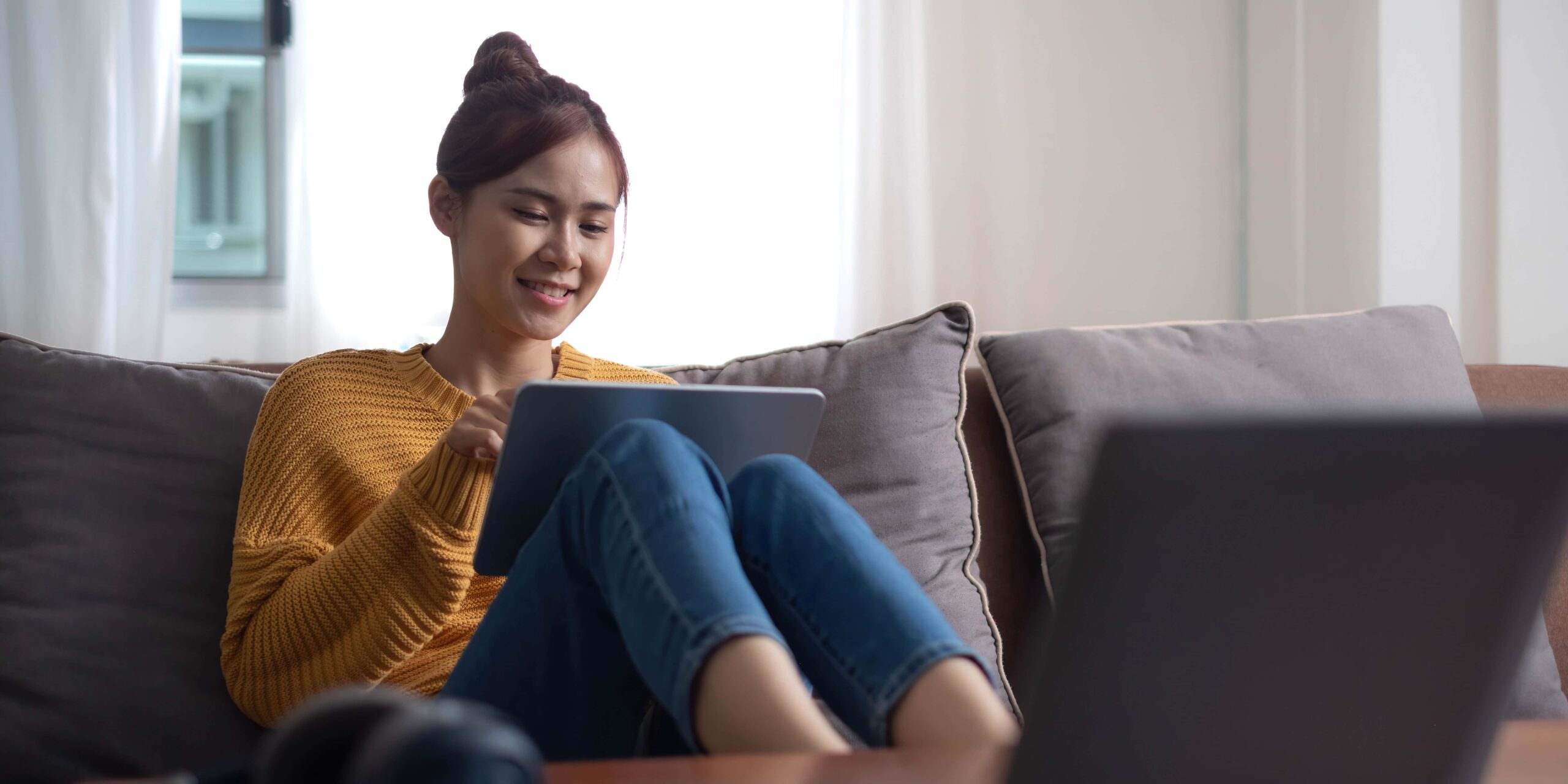 Candid of asian woman using tablet for watching online movie stream mobile device on sofa at living room. Young happy girl enjoying with entertainment media online on weekend scaled
